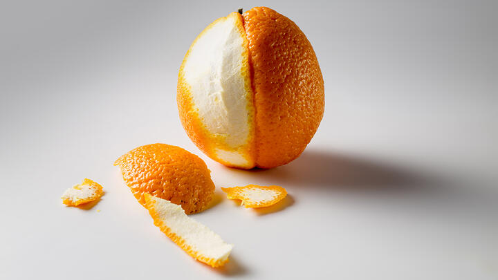 A photo of a half-peeled orange on a white surface