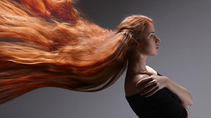 A beautiful young woman with very long ginger hair getting blown horizontally over to the left side of the screen