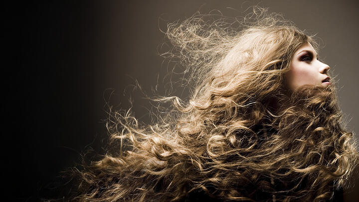A young blond woman in the spotlight on a dark background, with a gorgeous head of thick, wavy hair 